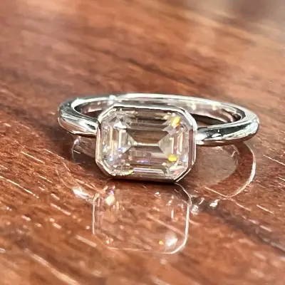 An-elegant-silver-ring-featuring-a-large-faceted-emerald-cut-stone-resting-on-a-polished-wooden-surface
